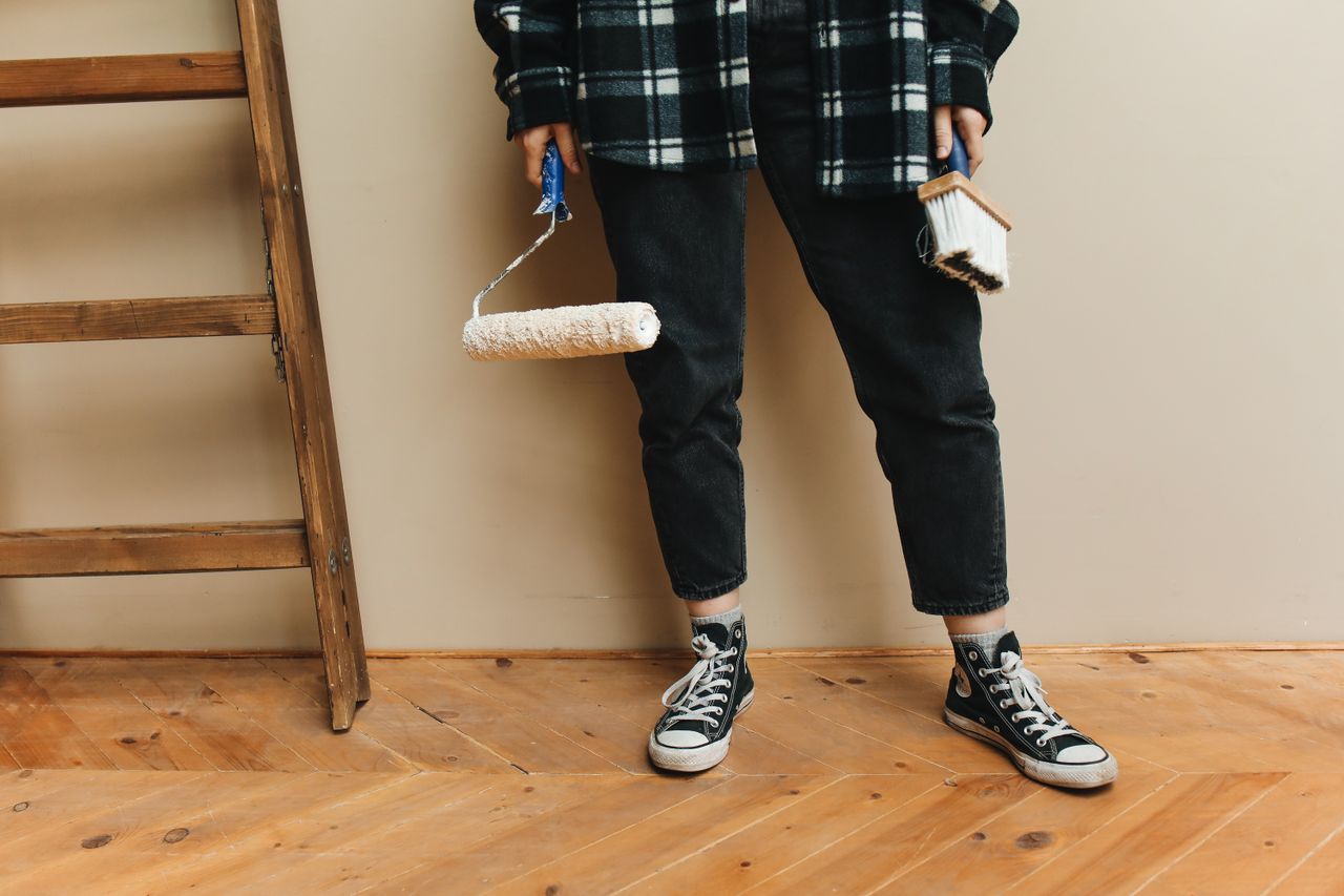 Une personne tenant un rouleau à peinture et un pinceau pendant un projet de rénovation de maison.