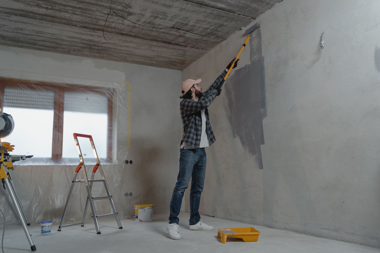 services-04 A man painting an interior wall with a roller during a home renovation project.